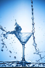 Splashing water on blue background. Cocktail glass with water.