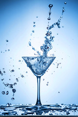Splashing water on blue background. Cocktail glass with water.