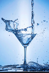 Splashing water on blue background. Cocktail glass with water.