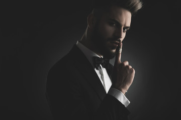 man in tuxedo hushing with finger at lips
