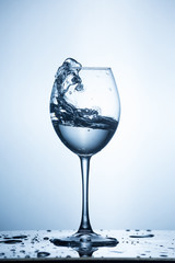 Splashing water on blue background. Wine glass with water.