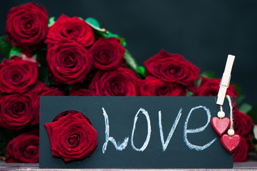 Concept Valentine day, the word love written in chalk on a plate on a background of a pile of red roses. Stylish love concept