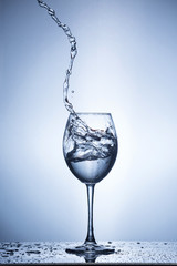 Splashing water on blue background. Wine glass with water.