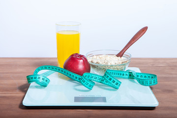 The concept of healthy diet, fitness and weight loss. Scales, measure tape, oatmeal, apple, a glass of juice on the table.