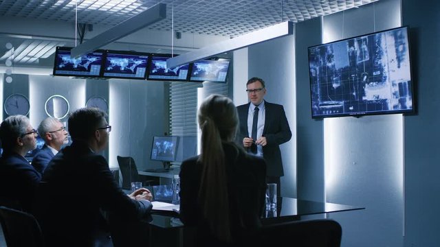 Special Agent in Charge Shows Satellite Surveillance Footage of the Car Getaway to a Team of Government Agents. GPS Tracking Fugitive in the Big Monitoring Room Full of Computers with Animated Screens