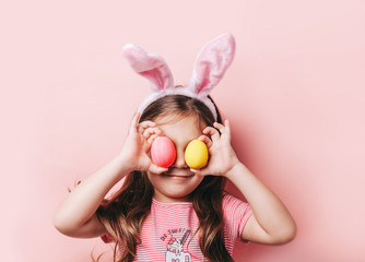 Cute little girl with bunny ears on pink background. Easter child portrait, funny emotions,...