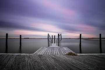 An empty peaceful dock within a marina as clouds streak across the sky. Still water, serene and...