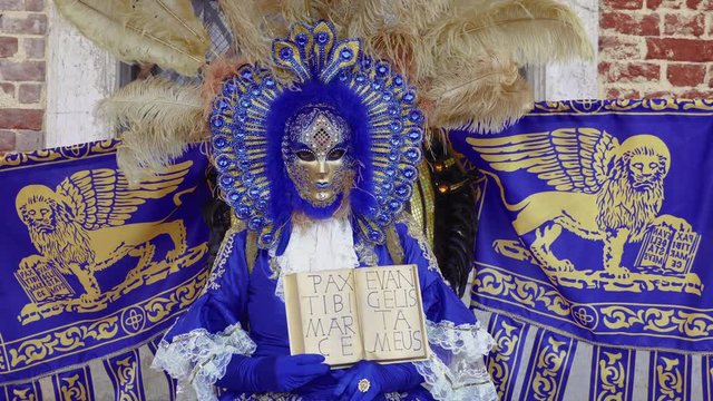 Venice, Italy Carnival mask and costume pose with Venetian Coat of Arms. Masked person in traditional costume poses with Venice Lion symbol and words Pax tibi Marce, Enangelista meus. 
