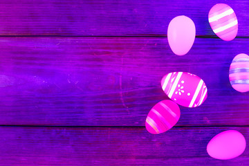 Pink and purple Easter eggs on a purple wooden table. Top view, copy space.
