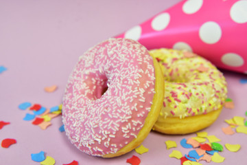 ein gelber und ein rosa donut mit konfetti und einem geburtstagshut vor rosa hintergrund