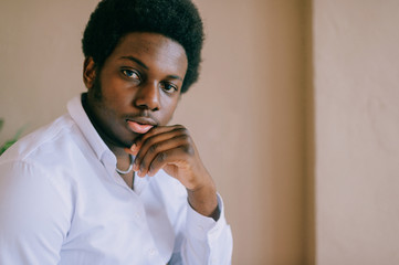 Closeup lifestyle toned portrait of young handsome dark-skinned african american confident man looking at camera on pink wall background. Indoor soft focus portrait of nigerian male in striped shirt.