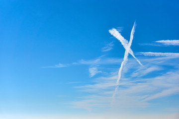 White clouds as an x shape sign against a saturated blue sky with copy space on the left   