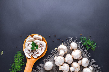 Fresh sliced champignon with parsley in wooden spoon and dill, white ripe mushrooms on a black background for cooking homemade delicious dishes. Copy space