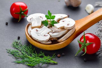 Fresh sliced white champignon in wooden spoon. Cooking homemade dishes of ripe mushroom with parsley, dill and tomatoes cherry