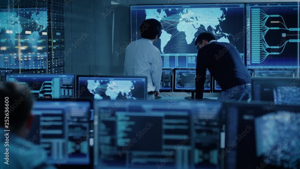 Poster In the System Control Room Project Manager and IT Administrator Have Discussion. Monitoring Station Has Capacity for Global Data and Monitoring, Every Interaction is Shown in Real Time on Displays