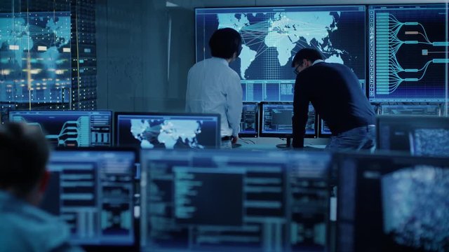 In the System Control Room Project Manager and IT Administrator Have Discussion. Monitoring Station Has Capacity for Global Data and Monitoring, Every Interaction is Shown in Real Time on Displays