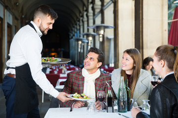 polite waiter serving guests at terrace restaurant