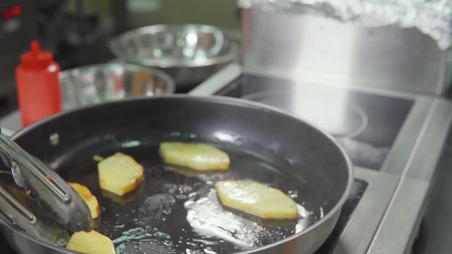 Cook frying sliced potato on frying pan in oil.