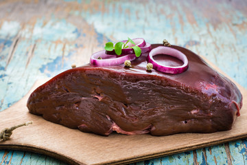 A piece of raw beef liver on a cutting board on a wooden table