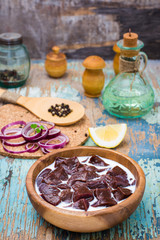 Pieces of raw beef liver soaked in milk in a wooden bowl and ingredients for cooking on the table