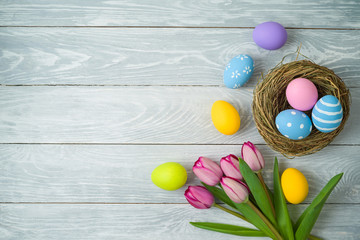 Easter holiday background with easter eggs in bird nest and tulip flowers on wooden table