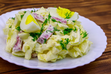 Salad with chinese cabbage, onion, sausage, eggs and mayonnaise on wooden table