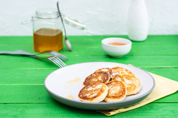 Ready-to-eat sweet cottage cheese pancakes with honey on a plate on a wooden table