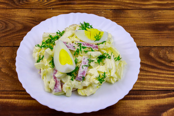 Salad with chinese cabbage, onion, sausage, eggs and mayonnaise on wooden table