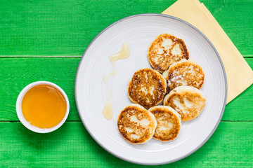 Homemade cottage cheese pancakes with honey on a plate on a wooden table. Top view