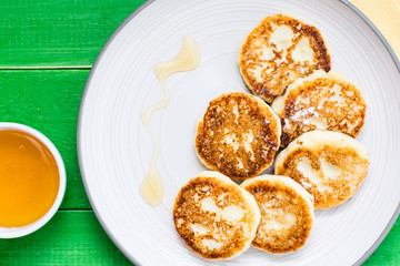 Close-up of homemade cottage cheese pancakes with honey on a plate on a wooden table. Top view