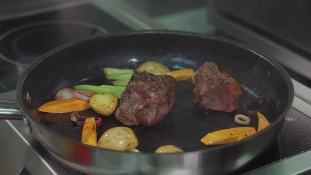 Frying vegetables and meat on a pan.