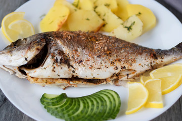 Baked dorada with potatoes on a white plate.