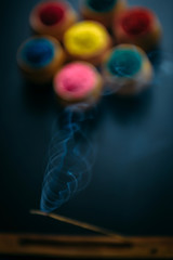 Burning and fuming aroma stick against circle of Holi powder in clay cups. Black background.  Happy...