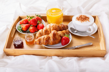 breakfast tray in bed : cup of cappuccino, juice, croissants and fresh strawberries