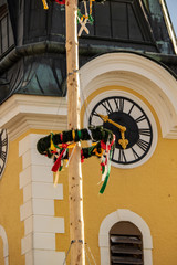 View of a church tower in the background with a maypole in the foreground. The maypole is one of...