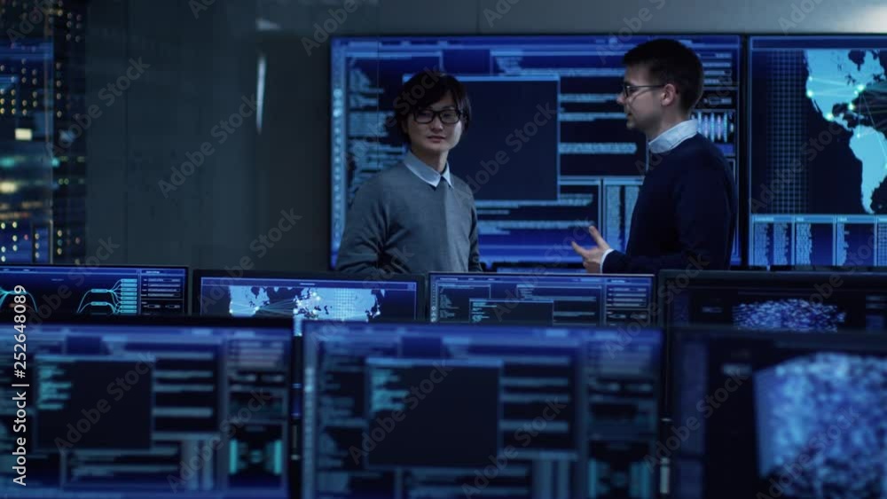 Poster In the System Control Room Project Manager and IT Administrator Have Discussion. Monitoring Station Has Capacity for Global Data and Monitoring, Every Interaction is Shown in Real Time on Displays