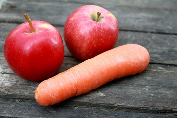 Beautiful fresh juicy ripe orange carrots and two red apples lay on the table summer