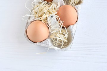 Easter eggs in carton box with straw on neutral wooden background. Brown chicken eggs on container with decorative straw elements for traditional Easter holiday