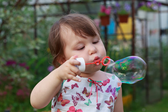 Cute little girl is blowing a soap bubbles.