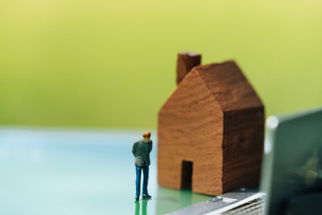 Concept for property ladder, mortgage and real estate investment. Miniature people: small figure standing in front of wooden house.