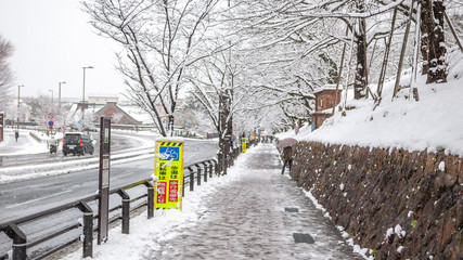 Lone man walking on an icy street during a rare snowfall in Kyoto city with a yellow signboard stating 