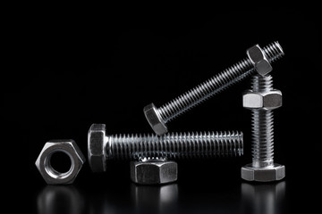 Bolts and nuts of different sizes on a black background. Still life with steel bolts and nuts.