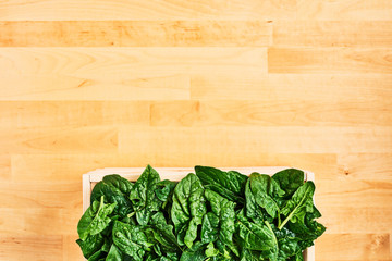 Fresh spinach leaves with water drops in wooden box on wooden table. Top view with copy space for text.