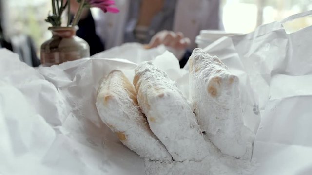 Slow motion shot of fresh powdered sugar coated fried dough beignets dessert on the table at a trendy cafe.