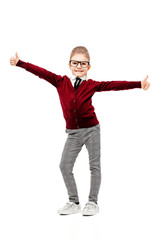 Beautiful little girl dressed like a School girl - in white shirt, red blouse and gray pants, rounded glasses standing near white wall and posing thumbs-up like model.