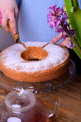 Sponge cake sprinkled with sugar powder. Woman is cutting a cake into pieces