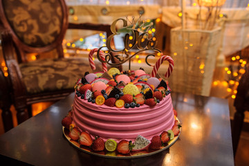 close up photo of a pink bithday cake decorated with fruits, candies and macarons for a little girl