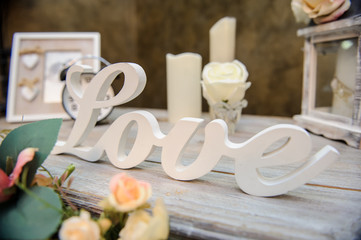 closeup photo of a wedding decor: a vintage wooden table with a flower arrangement, photo frame, candles, lamps, white inscription love on it