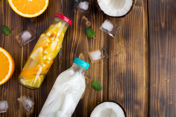 Detox water with coconut and orange in the glass bottles on the  brown wooden background.Top view.Copy space.