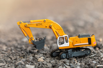 Yellow excavator model toy performs excavation work and load a gravel stone on a construction site....